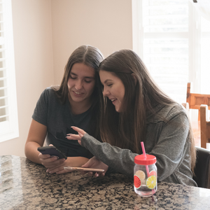 Two people sitting and scrolling through a phone smiling at a kitchen counter.